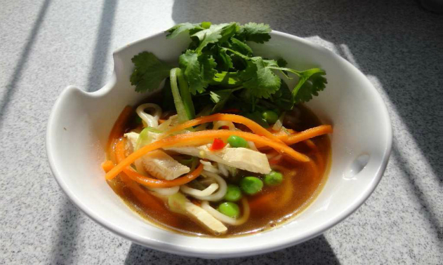 Bowl of chicken noodle soup with vegetables and a coriander garnish