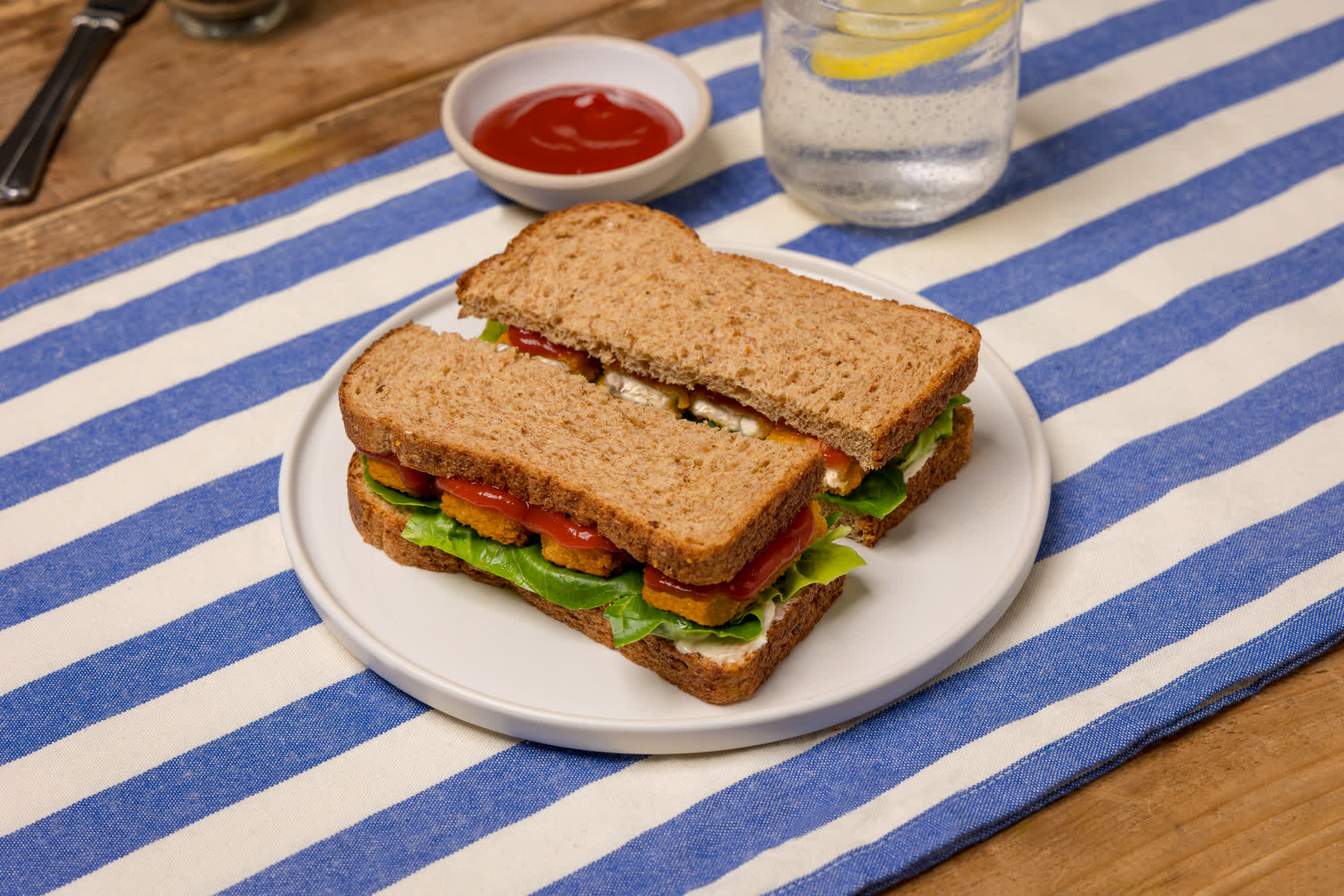 Fish finger sandwich sliced vertically down the middle, with ketchup, lettuce and tartar sauce