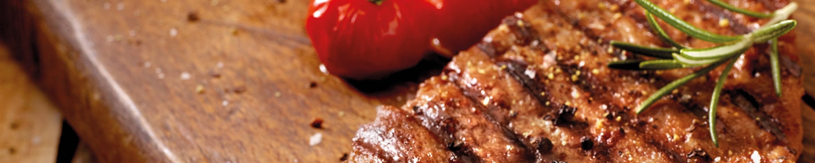 Grilled steak with rosemary and a roasted tomato on a wooden board